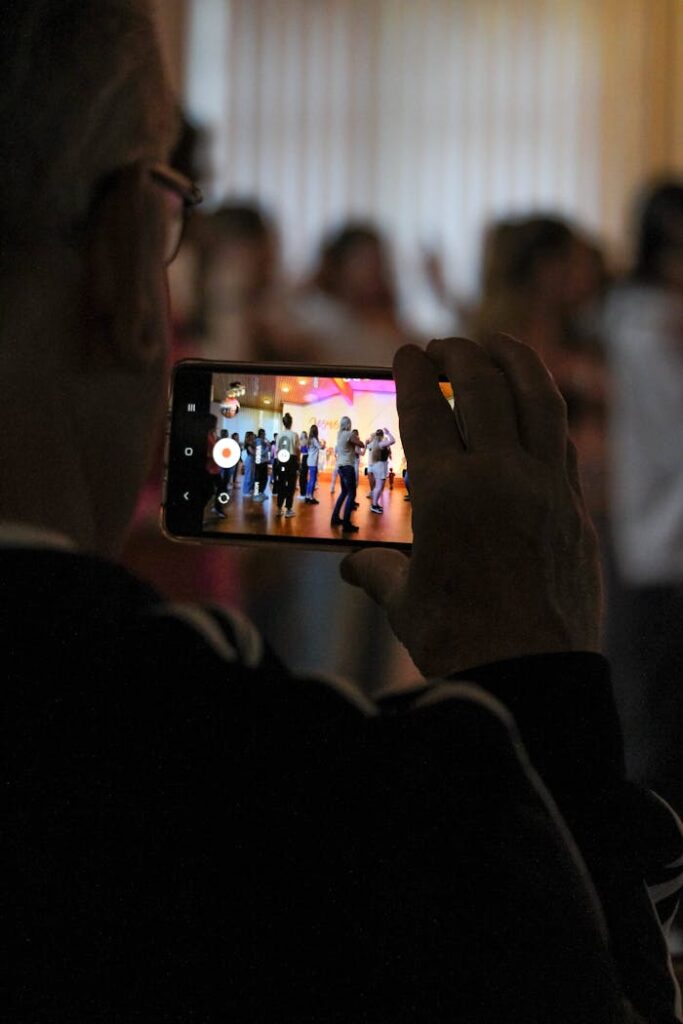 Senior adult recording a vibrant dance show using smartphone indoors.